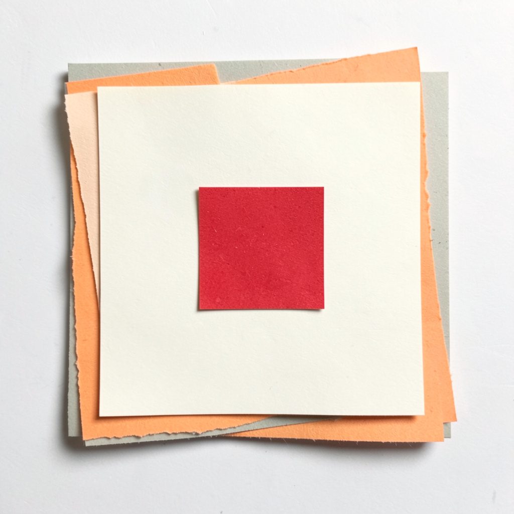 Square paper cut-out in cream with a single red square accent.